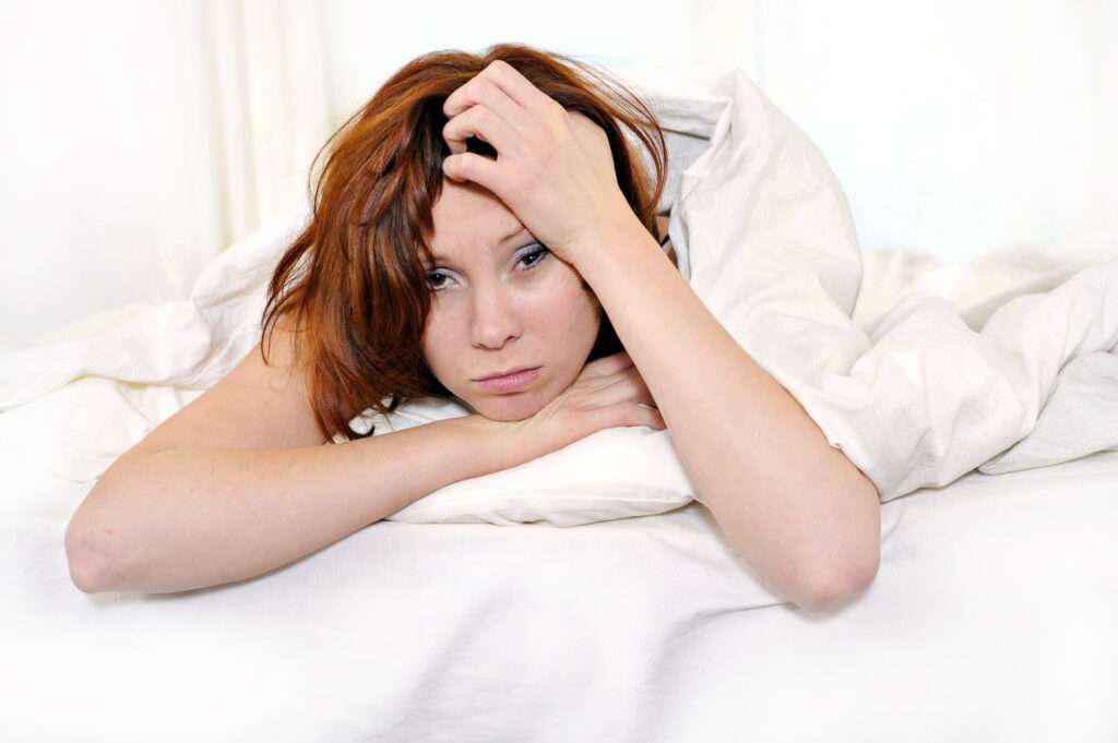 How Seasonal Changes Affect Your Sleep with a woman laying in bed looking exhausted and unable to sleep..