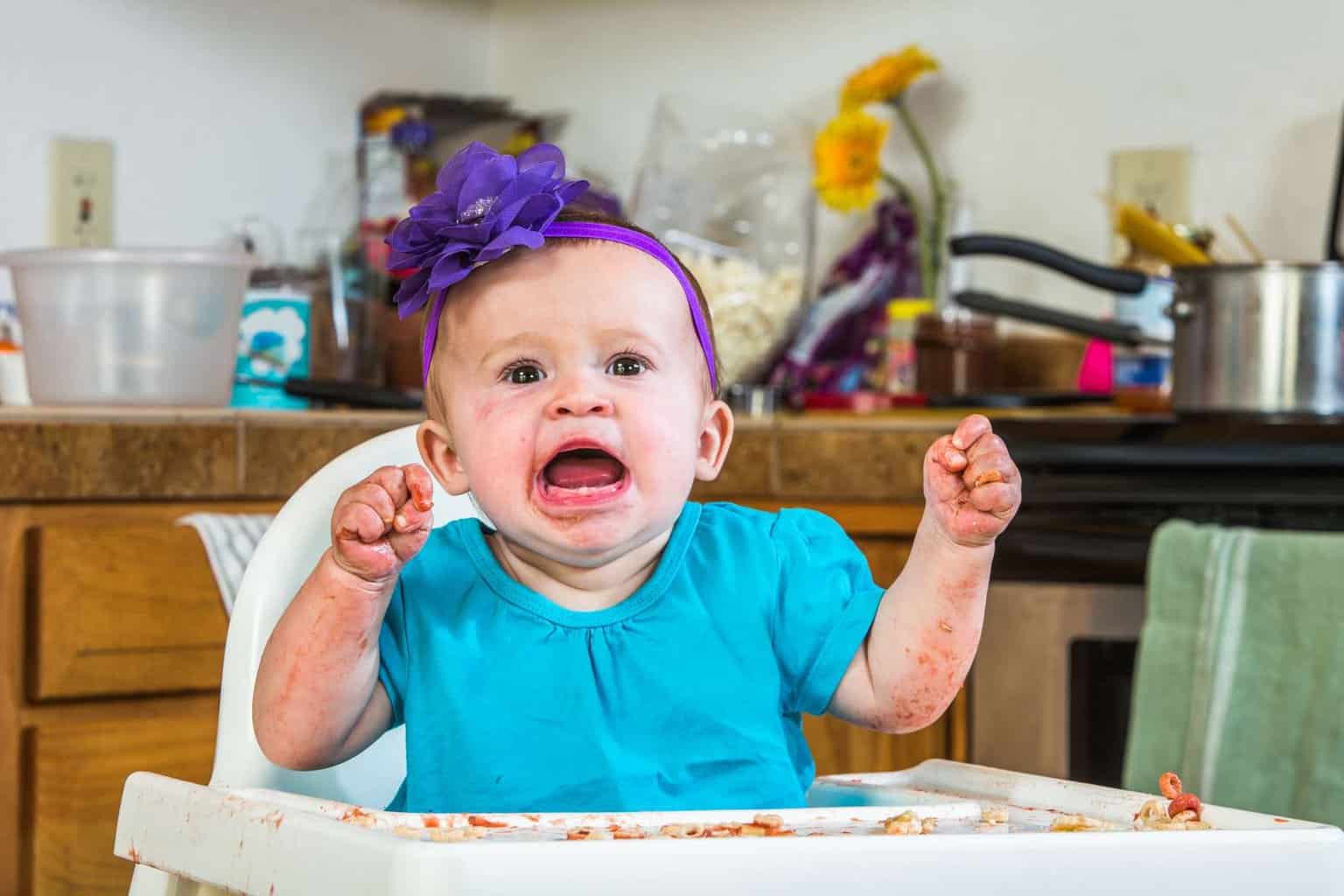 A baby experiencing holiday meal stress in a high chair with food on her face.