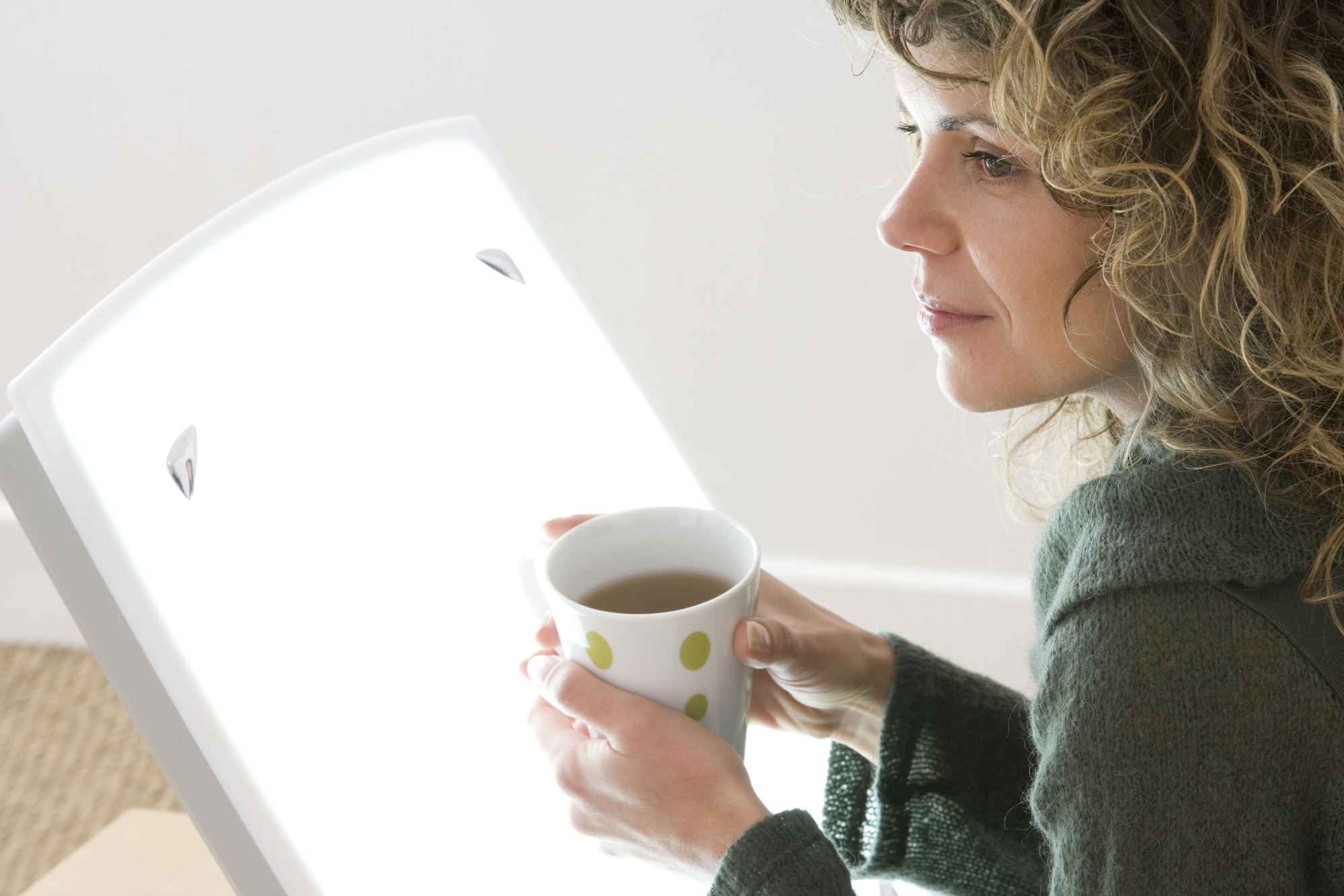 A woman enjoying a cup of coffee in the soothing glow of light therapy.